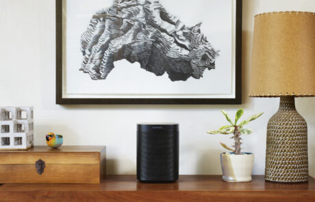 SONOS One Standlautsprecher steht in einem Wohnzimmer auf einem Regal.