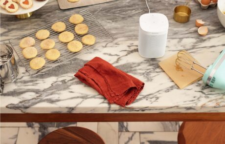 Der SONOS One steht in weiß auf einem Küchentisch, wo gerade Backwerk zubereitet wird.